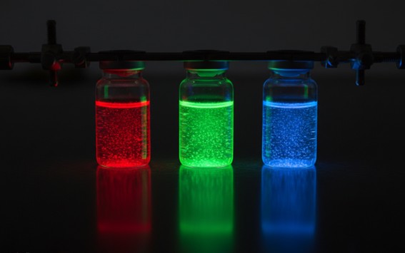 Glass vials of colloidal quantum dots show size-tunable red/green/blue fluorescence under UV light.