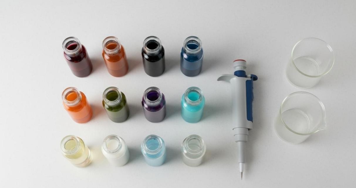 Neatly arranged glass vials with variously colored surface-functionalized nanoparticle dispersions alongside a pipette and beakers