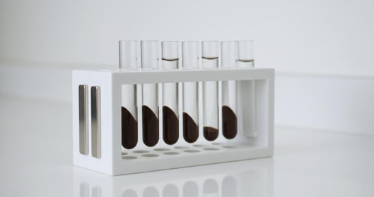 A white magnetic separator rack holding microcentrifuge tubes with dark magnetic particles attracted to the side walls.