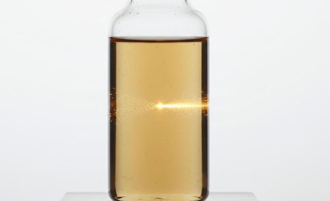 A clear glass vial containing brown-yellow aqueous graphene oxide dispersion showing the Tyndall effect.